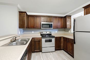 kitchen with a refrigerator, microwave, stove, and brown wooden cabinets at The Meadows Apartments in Florence, AL